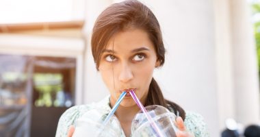 Young woman smiling and drinks two cocktails with ice in plastic cups with straw on city street.
