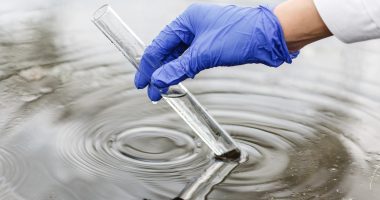 Researcher holds a test tube with water in a hand in blue glove